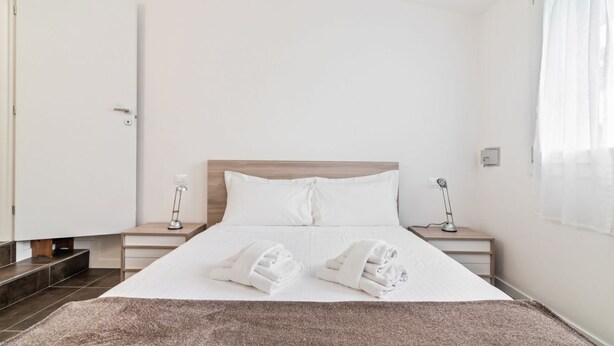 A hotel room with a bed, two bedside tables, a nightstand, a window with curtains, and a door.