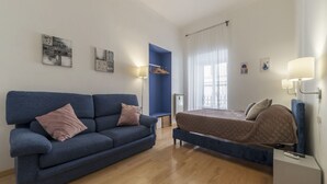 A modern room with a blue sofa, a bed, a small table, and artwork on the walls. - GuestHost - The quiet apartment is located on the first floor of a characteristic period building with a lift (NOT suitable for the disabled).In 55 square meters of space it accommodates 4 people, with two bedrooms.Located in the heart of the Prati distr (Roma)