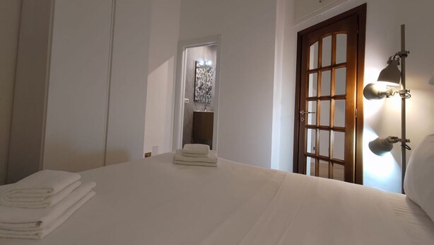 A bedroom with a bed, a nightstand, a lamp, a door, and a view of a bathroom. - GuestHost - The quiet apartment is located on the first floor of a characteristic period building with a lift (NOT suitable for the disabled).In 55 square meters of space it accommodates 4 people, with two bedrooms.Located in the heart of the Prati distr (Roma)