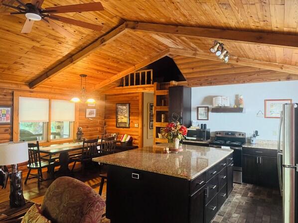 A cabin interior with a kitchen, dining area, and a ceiling fan.