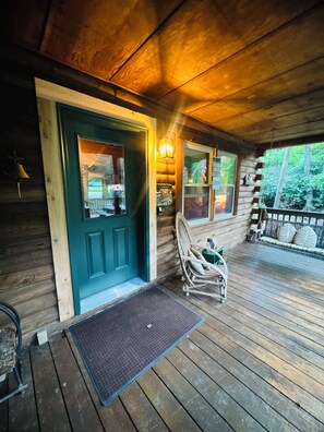 A wooden cabin with a front door, a porch with a rocking chair, and a view of the surrounding forest. - Our Little Slice of Heaven - Creekside Cabin on the Pacolet River (Saluda)