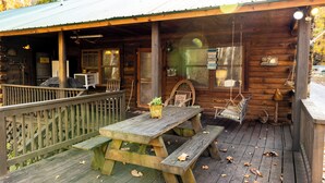 Een rustieke hut met een houten terras, picknicktafel en hangstoelen.
