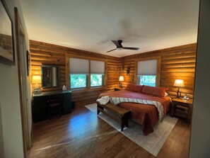 A log cabin bedroom with a bed, bedside tables, a desk, and a ceiling fan. - Our Little Slice of Heaven - Creekside Cabin on the Pacolet River (Saluda)