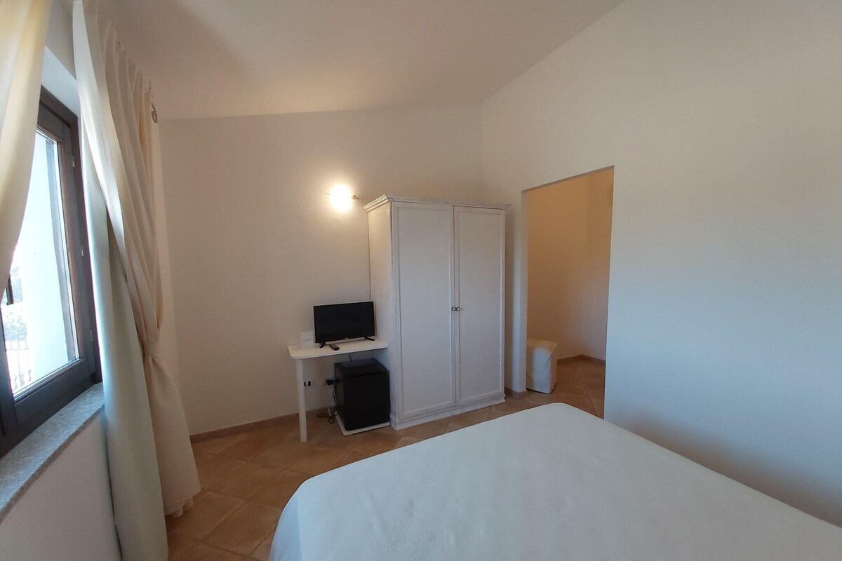 Une chambre à coucher avec un lit, une armoire, un bureau avec un ordinateur et une fenêtre avec des rideaux.