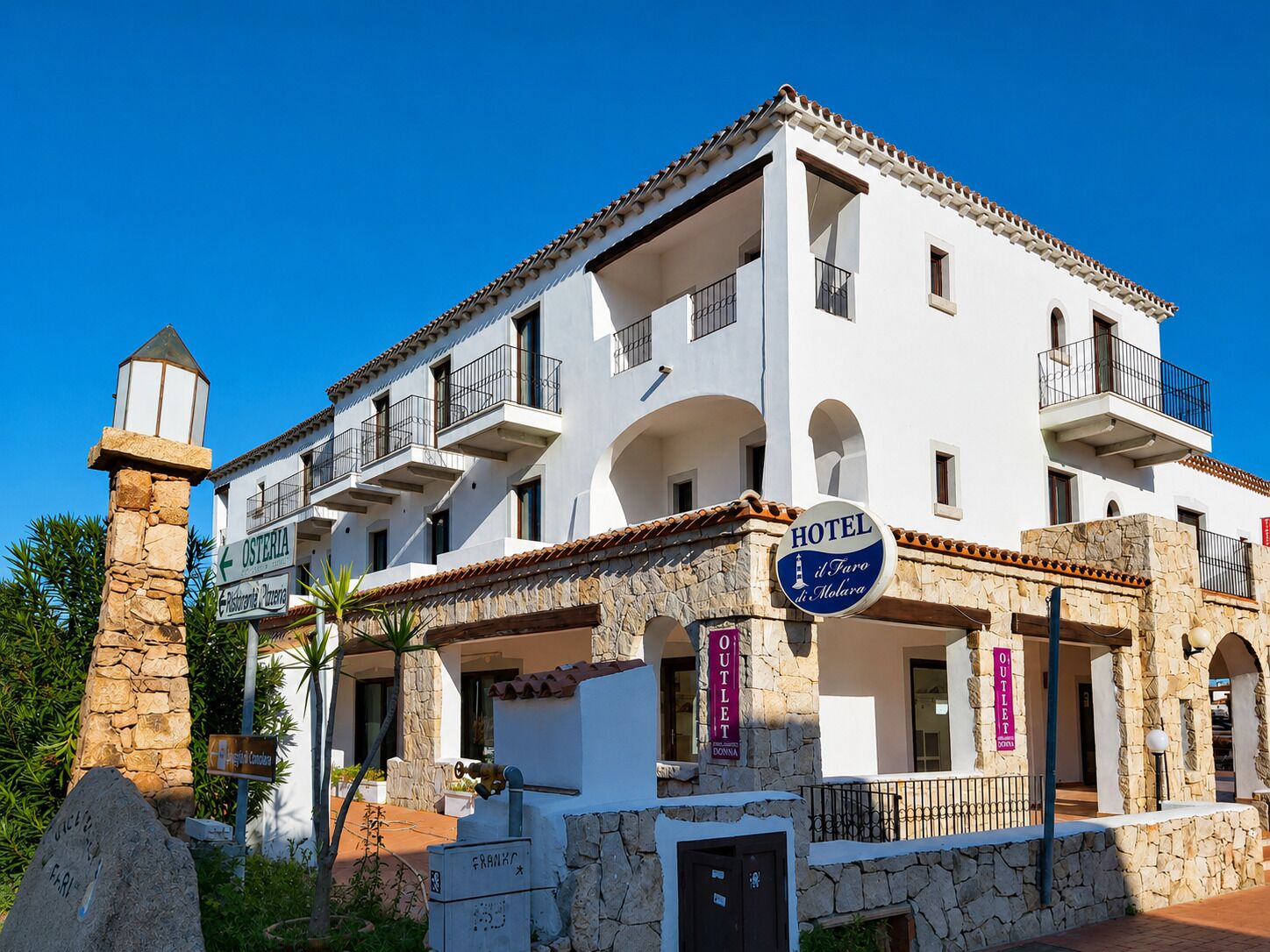 Un hotel a più piani con balconi, una facciata in pietra e indicazioni per un ristorante e un negozio.