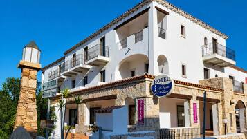 Un hotel a più piani con balconi, una facciata in pietra e indicazioni per un ristorante e un negozio.