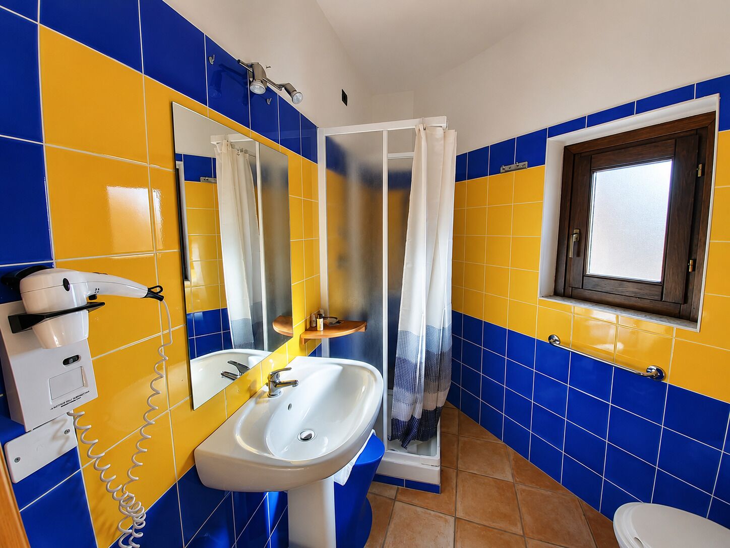 Une salle de bain avec un lavabo blanc, un miroir, une douche avec un rideau et une fenêtre avec un cadre en bois.