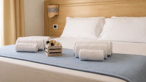 A hotel room with a bed, two rolled towels, a wooden tray with toiletries, and a blue throw blanket. - Hotel Il Faro di Molara (Loiri Porto San Paolo)
