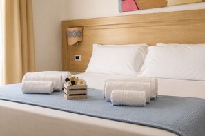 A hotel room with a bed, two rolled towels, a wooden tray with toiletries, and a blue throw blanket. - Hotel Il Faro di Molara (Loiri Porto San Paolo)
