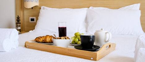 Cama arrumada com uma bandeja de itens de café da manhã, incluindo um croissant, uma tigela de cereal, uma xícara de café e um copo de suco.