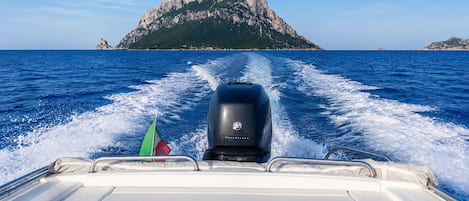 A boat's wake in the ocean with a rocky island in the distance.
