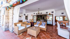 A spacious living area with wicker furniture, a bar area, and a view of the sea. - Hotel Il Faro di Molara (Loiri Porto San Paolo)
