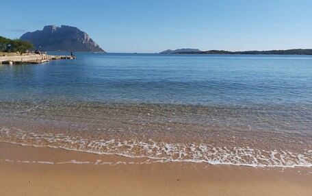 A beach with clear water, a sandy shore, and distant mountains.
