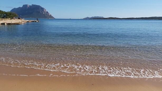 A beach with clear water, a sandy shore, and distant mountains. - Hotel Il Faro di Molara (Loiri Porto San Paolo)