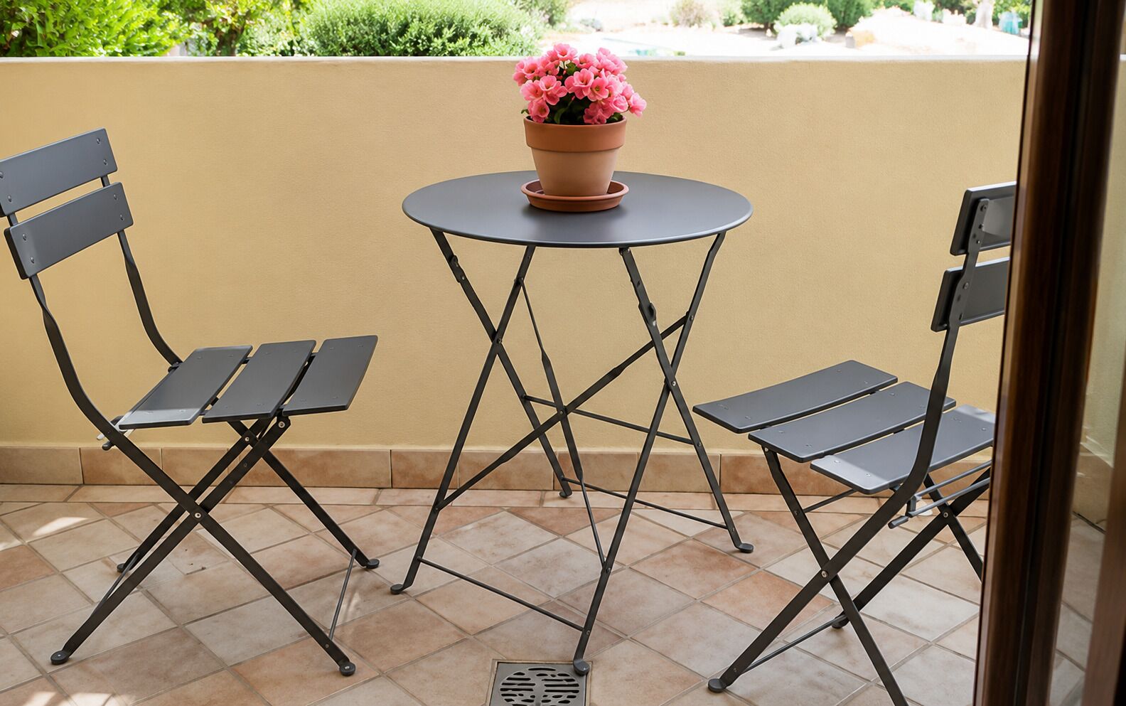 Une terrasse avec deux chaises et une table, une plante en pot posée sur la table, et un mur beige en arrière-plan.