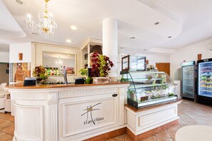 Un vestíbulo de hotel con mostrador de recepción, un candelabro, un refrigerador y una vitrina con flores.