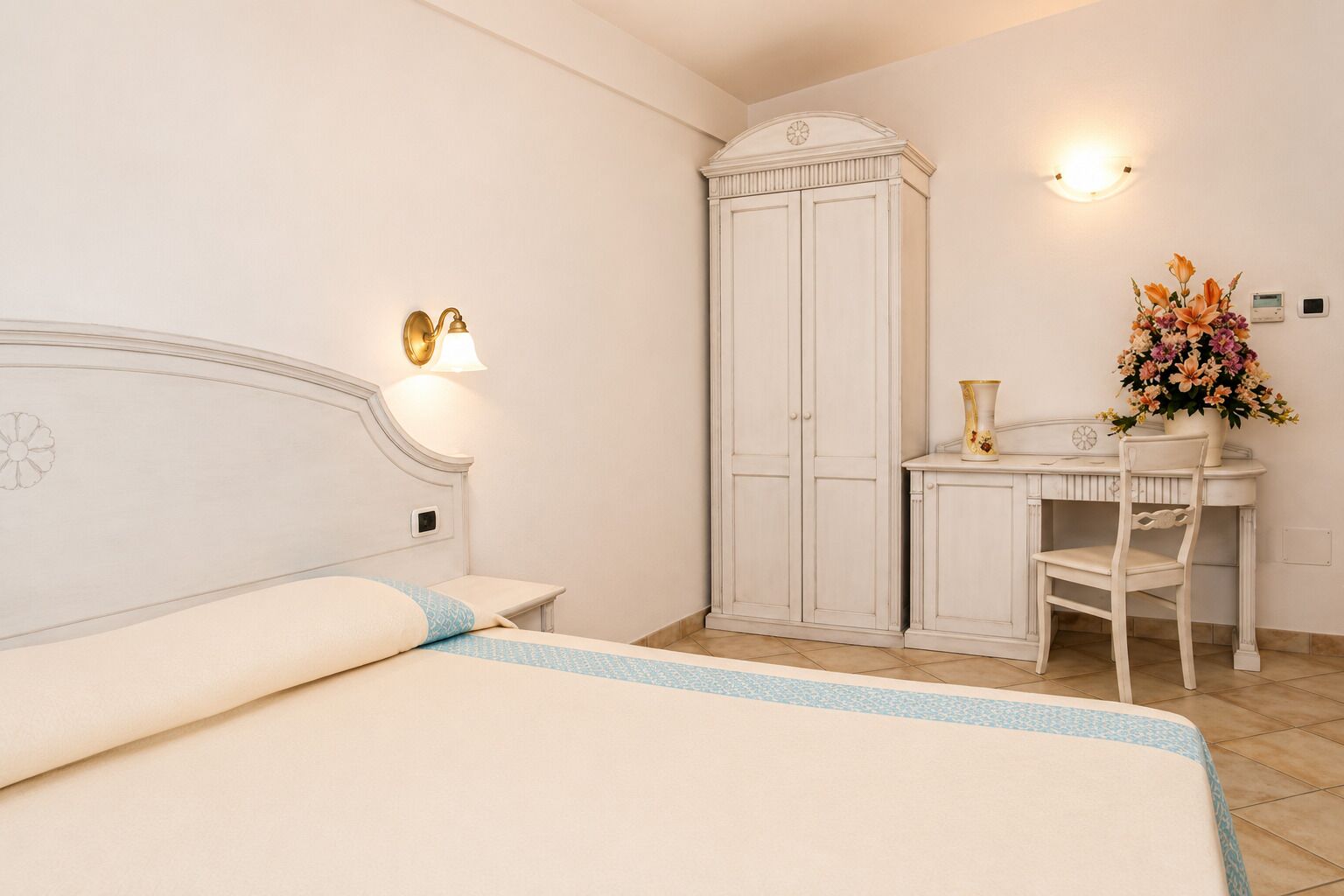 Un dormitorio con cama, armario, escritorio y silla, y un aplique de pared.