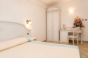 Ein Schlafzimmer mit einem Bett, einem Kleiderschrank, einem Schreibtisch mit Stuhl und einer Wandleuchte.