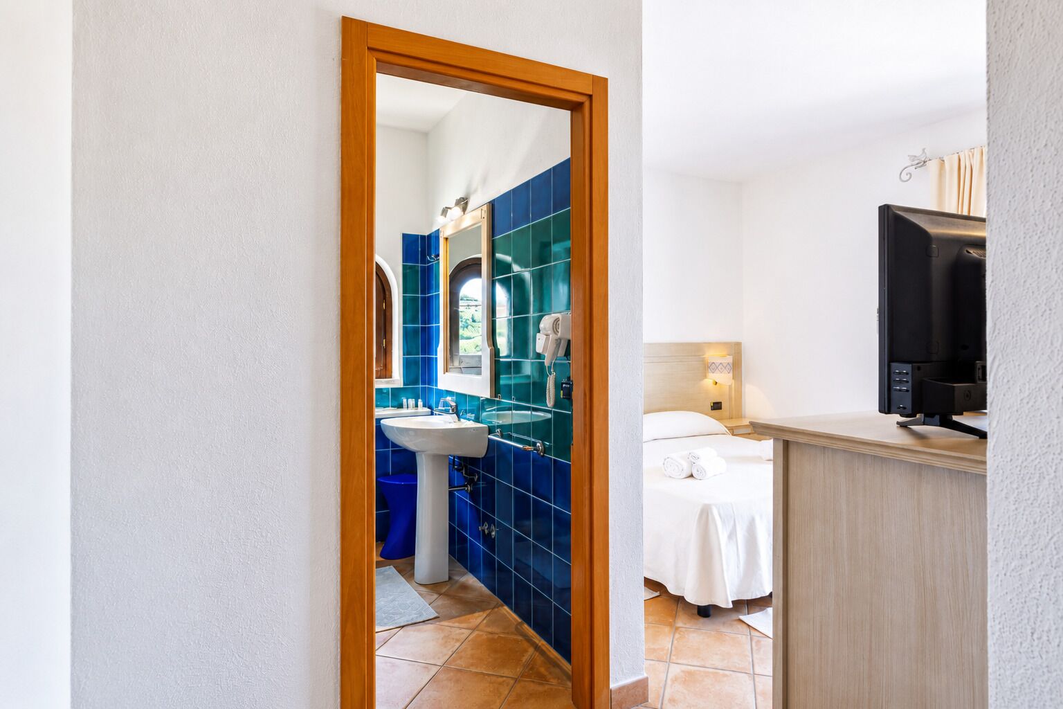 Une chambre d’hôtel avec une salle de bain carrelée de carreaux bleus, comprenant un lavabo et un miroir.