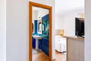Habitación de hotel con baño que presenta azulejos azules, un lavamanos y un espejo.