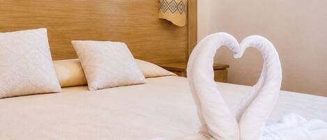 A bed with a wooden headboard, two pillows, and a towel arranged in the shape of a swan.