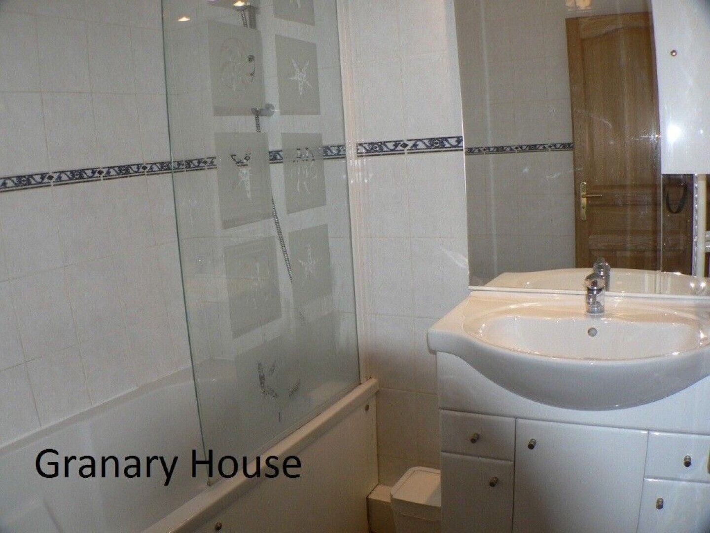 A bathroom with a glass shower enclosure, a white sink with a mirror, and a tiled wall with a decorative border.