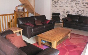 Ein gemütliches Wohnzimmer mit einer Holztreppe, einer Steinwand und einem schwarzen Ledersofa.
