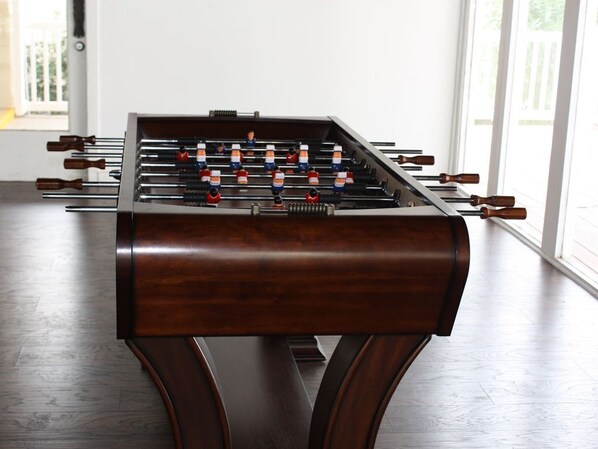 Una mesa de fútbol de mesa en una habitación con suelo de madera y ventanas amplias.