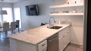 A modern kitchen with a marble countertop, stainless steel appliances, and white cabinetry.
