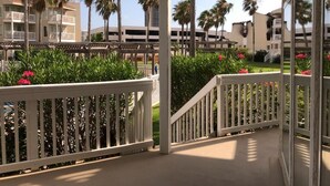 A covered outdoor area with white railings, palm trees, and a view of hotel buildings in the background.