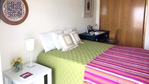 Ein ordentlich eingerichtetes Schlafzimmer mit Bett, Nachttisch, Lampe und einem gerahmten Bild an der Wand.