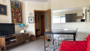 Ein Wohnzimmer mit Fernseher, einem roten Sofa, einem Esstisch mit Stühlen und Kunstwerken an den Wänden.
