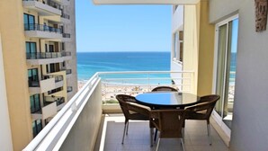 Ein Balkon mit Tisch und Stühlen mit Blick auf Strand und Meer.