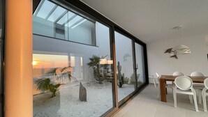 Ein modernes Interieur mit einer großen Glaswand, einer Essecke mit weißen Stühlen und einem Kakteengarten.