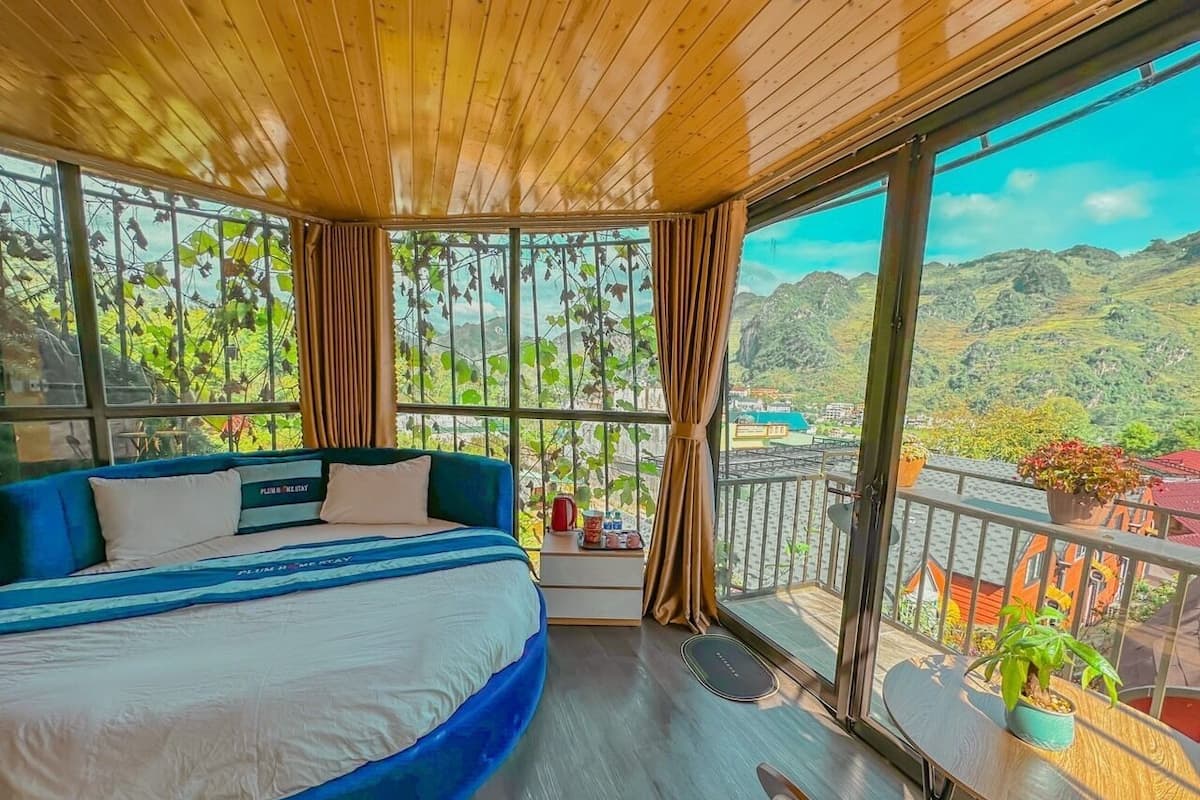 A bedroom with a large bed, a balcony with a view of the mountains, and a wooden ceiling.