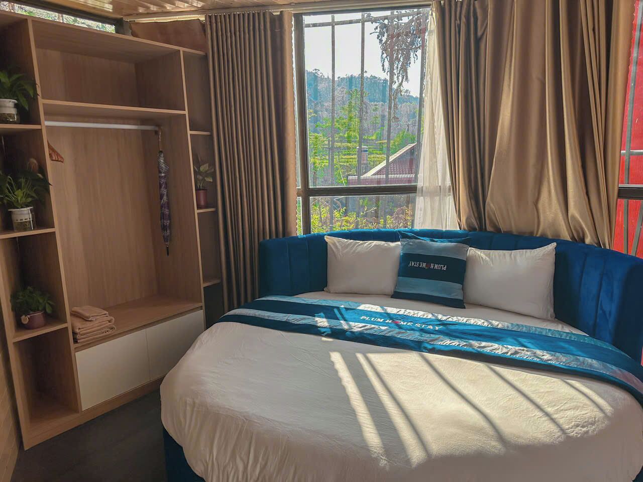 A bedroom with a bed, a wardrobe, a window with curtains, and a view of greenery outside.