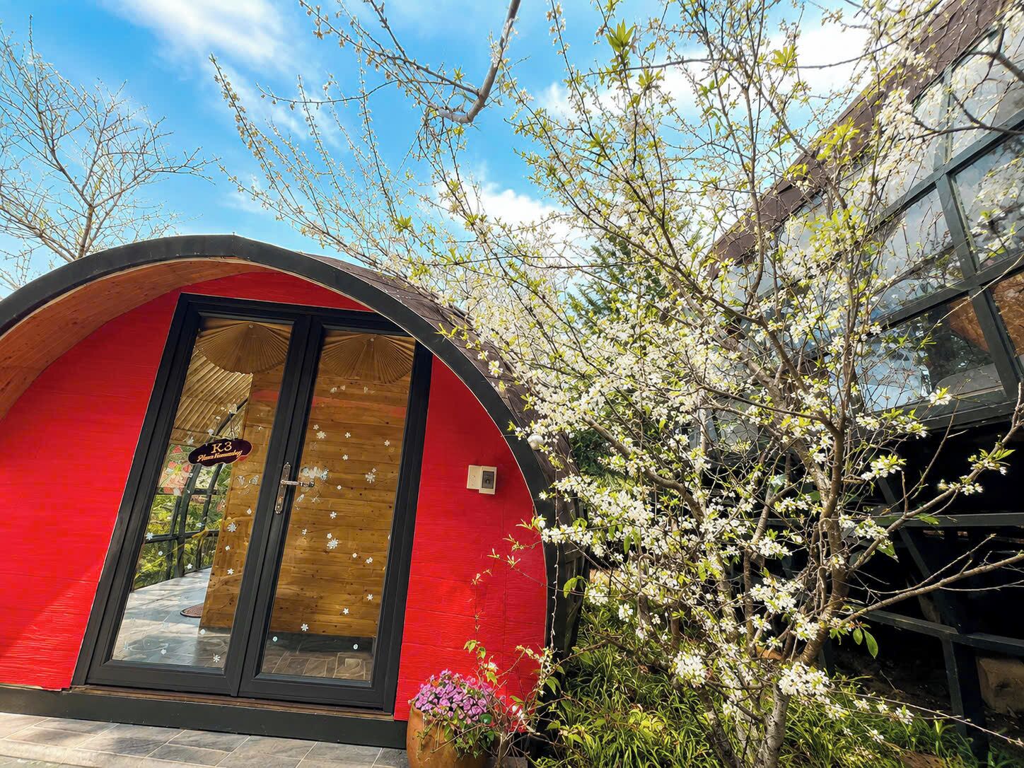 A red building with a large glass door, surrounded by blooming trees.