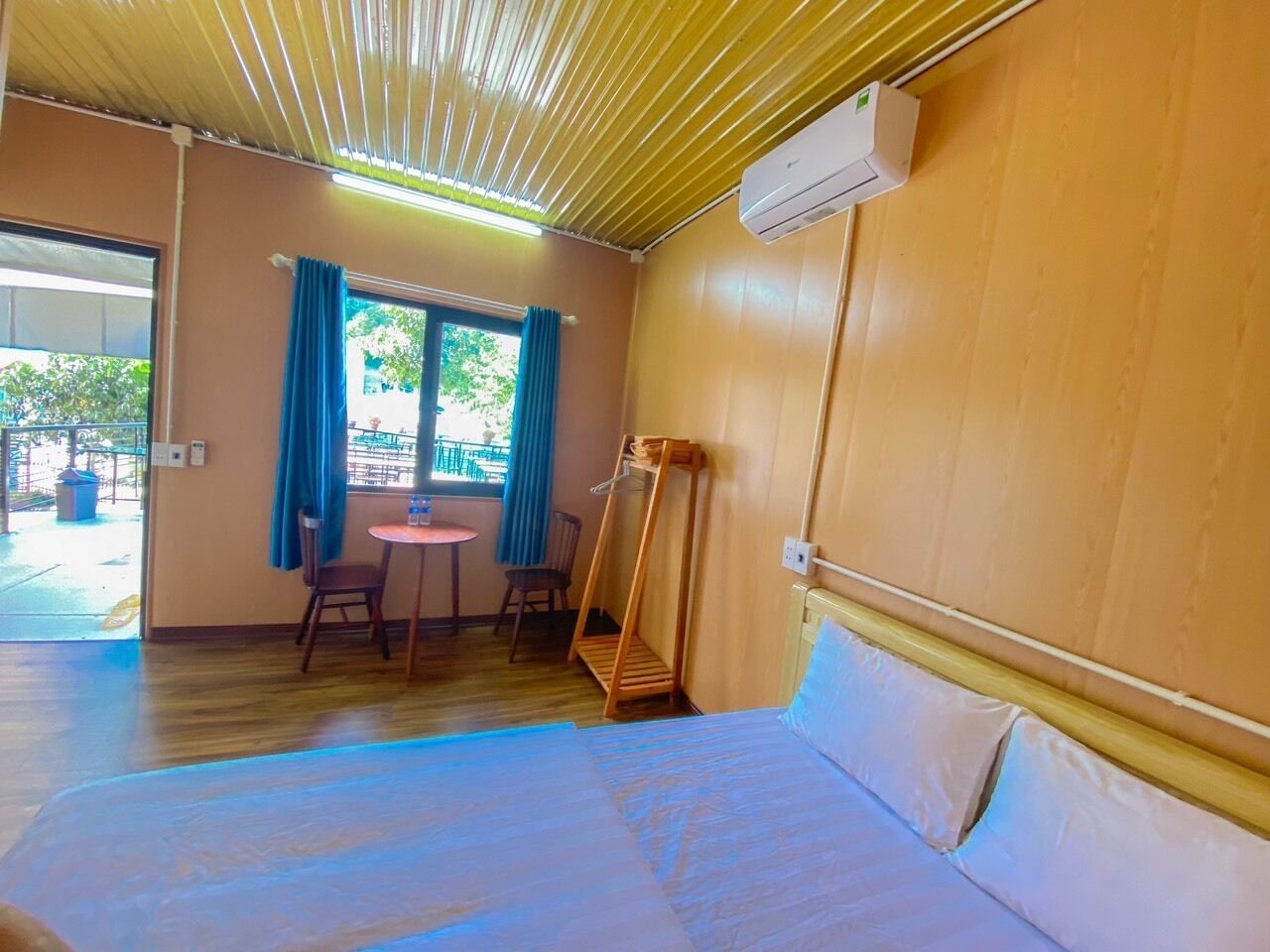 Une pièce comprenant un lit, une petite table, des chaises, une fenêtre avec des rideaux et un appareil de climatisation.