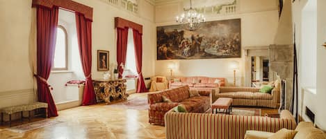 Une pièce spacieuse, ornée d’un grand tableau, de plusieurs canapés, d’un lustre et d’une cheminée.