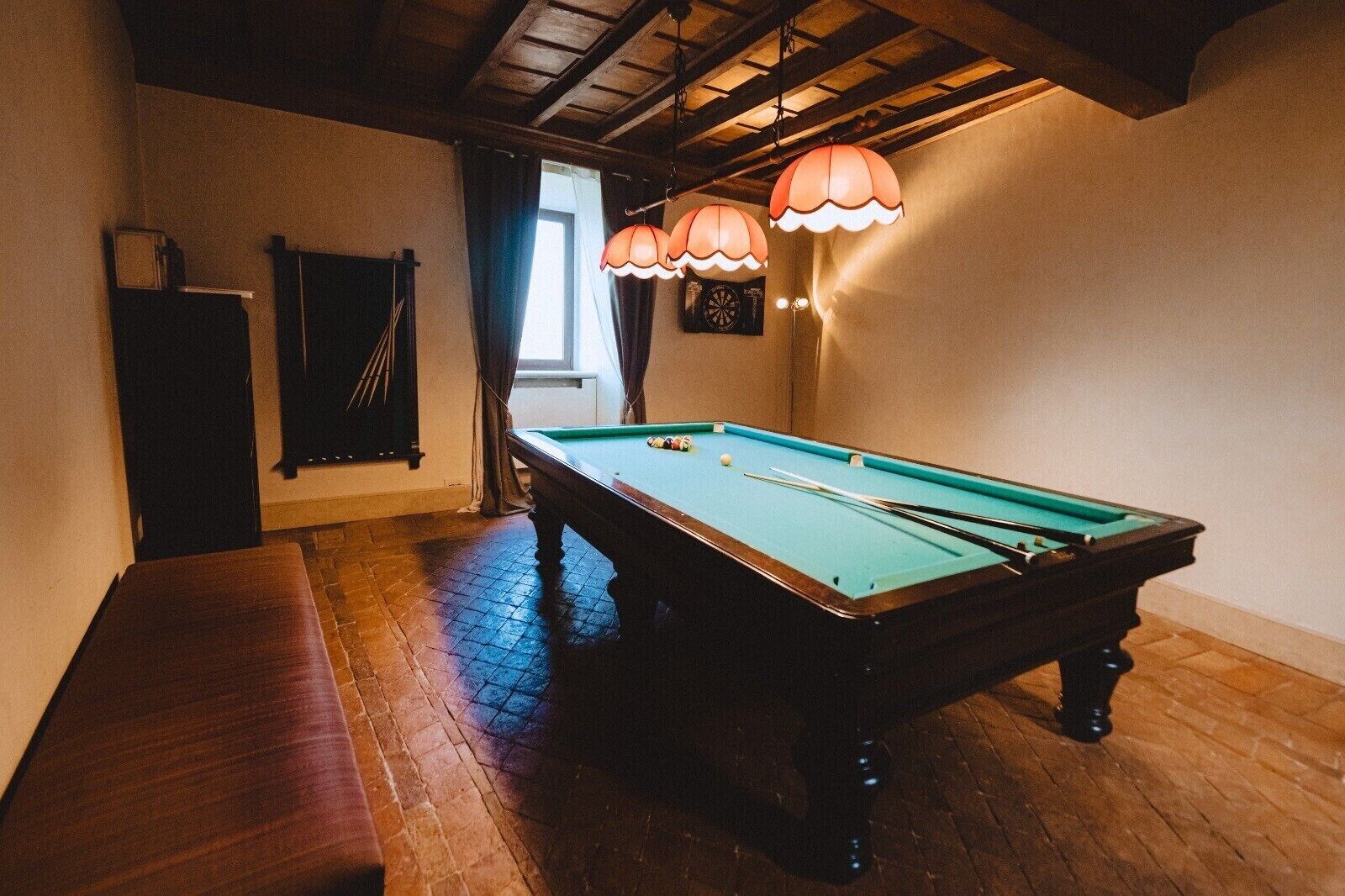 A pool table in a room with wooden flooring and a bench.