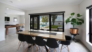 Un comedor moderno con una mesa grande y sillas, vistas a la piscina y una planta en maceta.