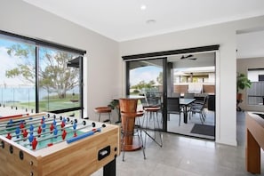 Un interior moderno con una mesa de fútbol, una zona de comedor con una mesa de vidrio y vistas amplias a través de grandes ventanales.