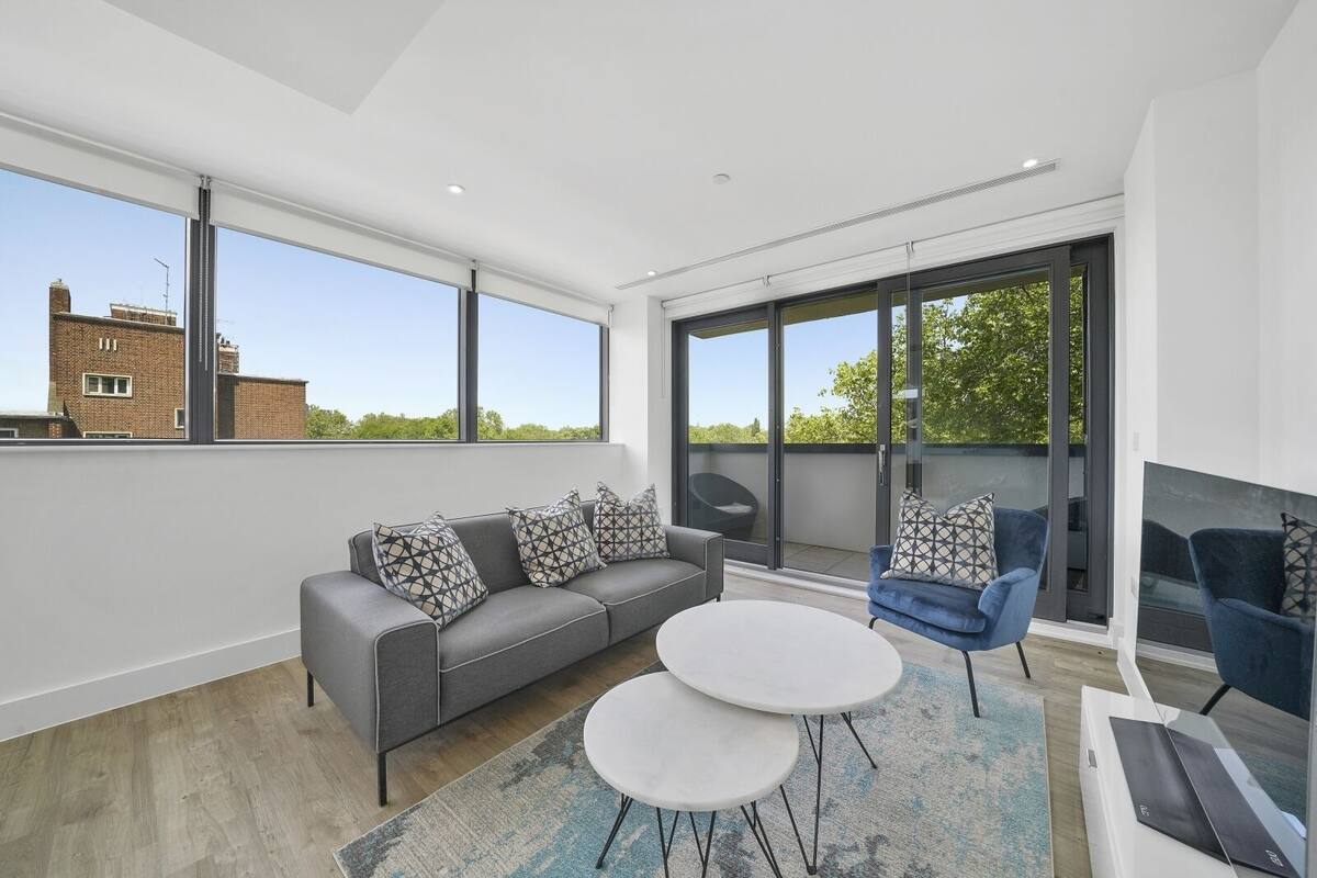 Un salon moderne avec un canapé gris, deux petites tables rondes blanches et un fauteuil bleu.