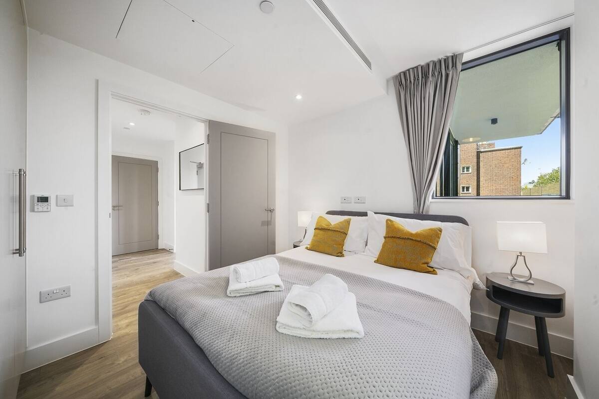 Une chambre d’hôtel moderne avec un grand lit, une table de chevet avec une lampe, un miroir et une vue sur l’extérieur.