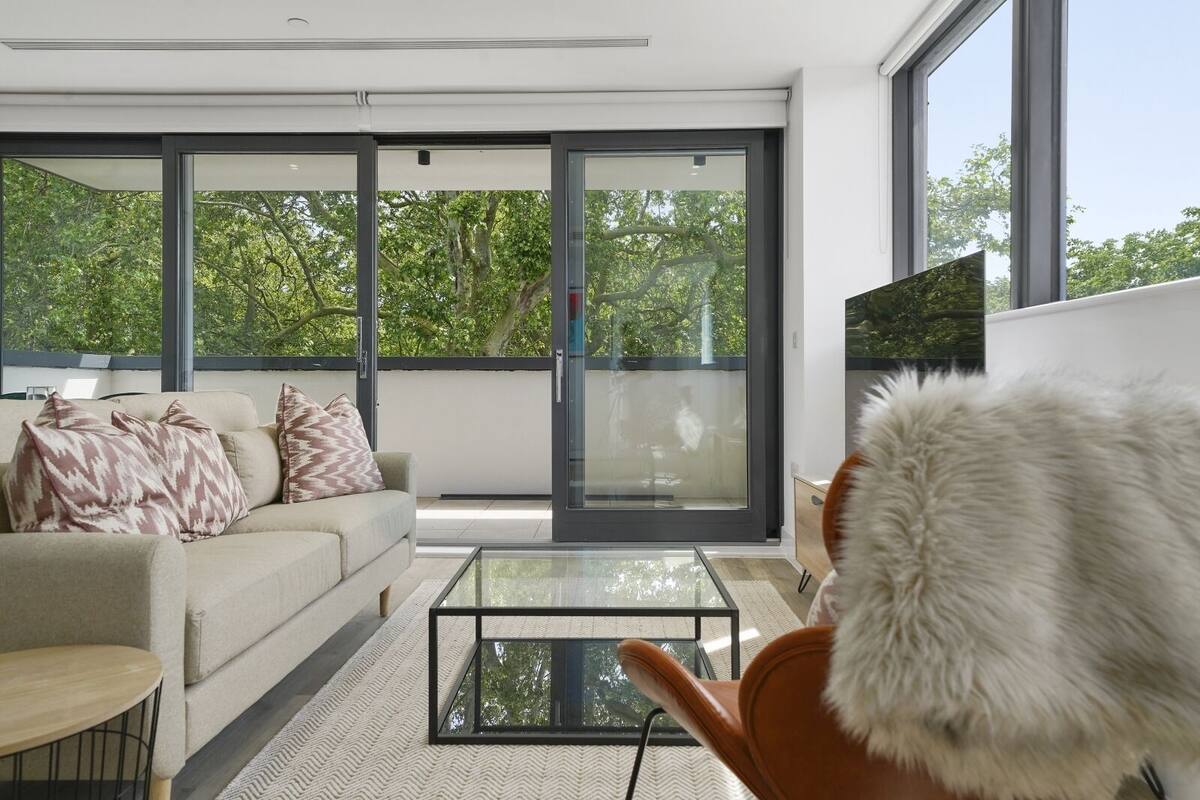 Un salon moderne avec un canapé, une table basse en verre et une vue sur les arbres, visible à travers de grandes portes-fenêtres coulissantes.