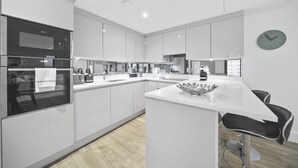 A modern kitchen with white cabinetry, stainless steel appliances, and a central island with bar stools. - Executive Apartments in Bermondsey FREE WIFI & AIRCON by City Stay Aparts London (London)