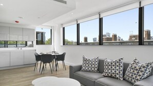 A modern living room with a grey sofa, patterned cushions, a dining table with chairs, and a kitchen area with a white countertop and cabinets. - Executive Apartments in Bermondsey FREE WIFI & AIRCON by City Stay Aparts London (London)