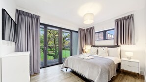 A modern bedroom with a large bed, bedside tables, a wardrobe, and a sliding glass door leading to a garden. - Executive Apartments in Bermondsey FREE WIFI & AIRCON by City Stay Aparts London (London)