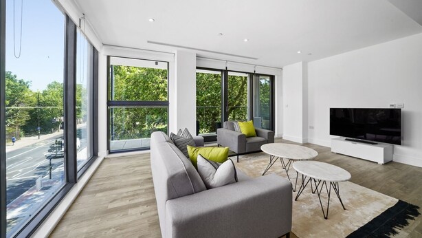 A modern living room with large windows, a grey sofa, a small round table, and a flat-screen TV. - Executive Apartments in Bermondsey FREE WIFI & AIRCON by City Stay Aparts London (London)