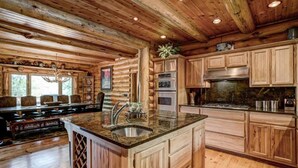 A log cabin interior with a kitchen featuring wooden cabinets, granite countertops, and a central island with a sink. - Luxury 7,500‑Sq‑Ft Lakefront Lodge, Private Dock & Snowmobile Access (Hayward)